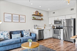 A modern kitchen with stainless steel appliances, a blue sofa, and decorative wall art. - Modern Updates, 1 Minute to the Beach!  + Free Attraction Tickets! (Santa Rosa Beach)