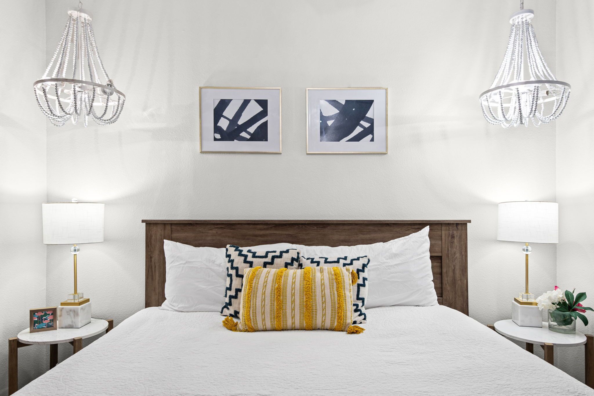 Habitación de hotel con una cama, dos candelabros fijos en la pared, dos obras de arte abstracto enmarcadas y lámparas de noche.