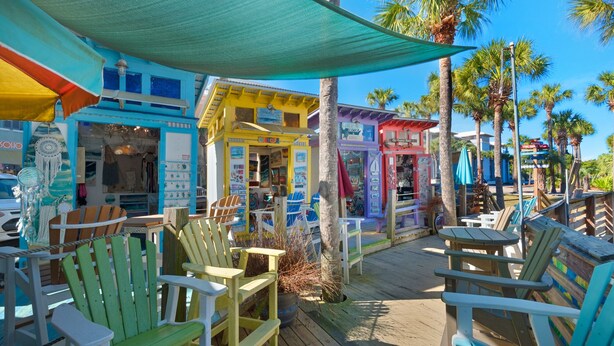 A colorful outdoor seating area with wooden chairs and tables, surrounded by buildings with various shops and signs. - Modern Updates, 1 Minute to the Beach!  + Free Attraction Tickets! (Santa Rosa Beach)