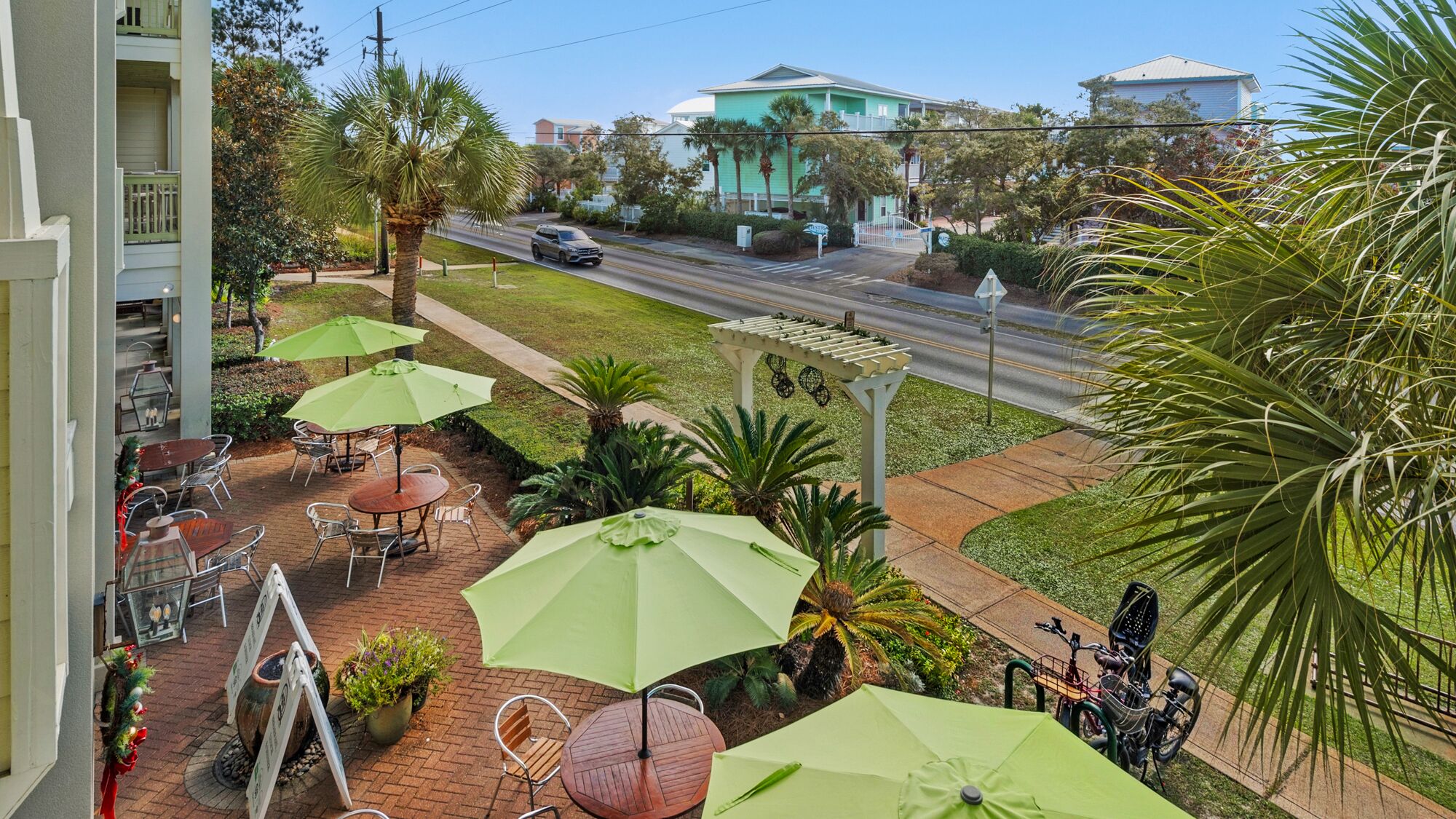 A balcony with outdoor seating, a pergola, and a view of a street with buildings and a car.