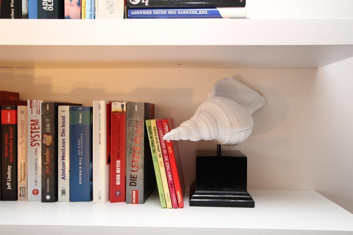 A bookshelf with various books and a white sculpture.