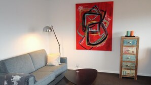 A modern living room with a grey sofa, a dark coffee table, a red abstract painting, a floor lamp, and a wooden cabinet with drawers. - Hussmann, Germany (Sylt)