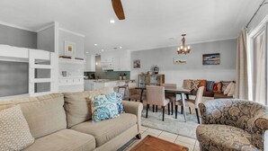 A modern living room with a beige sofa, patterned armchair, and dining area with chairs and a table.