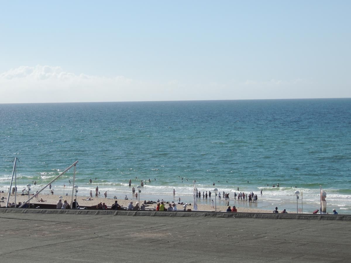 Una playa con un paseo marítimo de concreto y gente caminando por la orilla.