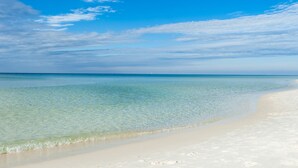 Ein Strand mit klarem, flachem Wasser und einem entfernten Segelboot.