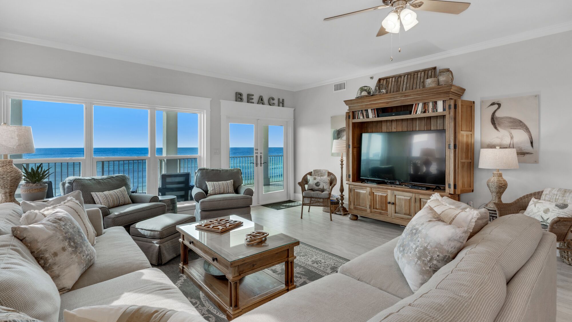 A spacious living room with a large TV, comfortable seating, and a view of the ocean.