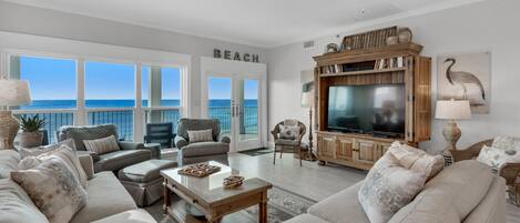 A spacious living room with a large TV, comfortable seating, and a view of the ocean.