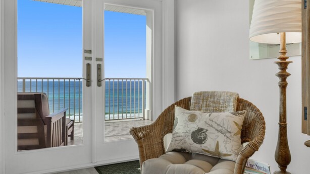 Ein Korbstuhl mit Kissen, eine Lampe und Blick auf das Meer durch eine Glastür.