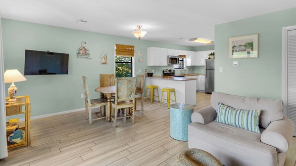 Una sala de estar con sofá y televisor, un comedor con sillas y mesa, y una cocina con refrigerador y estufa.