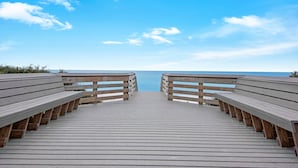 A wooden boardwalk leading to a beach with benches on either side.