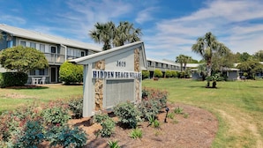 A sign for 'Hidden Beach Villas' with a number '3605' and a well-maintained lawn with various plants and a small tree.