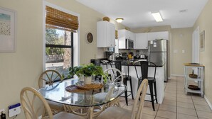 A modern kitchen with white cabinets, a stainless steel refrigerator, and a dining area with a glass table and wicker chairs. - Mins to Beach, 2 Pools & Tennis, Ground Floor Unit + Free Attraction Tickets! (Santa Rosa Beach)