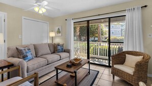 A living room with a sofa, a wicker chair, a coffee table, and a sliding glass door leading to a balcony. - Mins to Beach, 2 Pools & Tennis, Ground Floor Unit + Free Attraction Tickets! (Santa Rosa Beach)