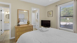 Une chambre à coucher avec un lit, une commode, une télévision et une fenêtre avec des stores.