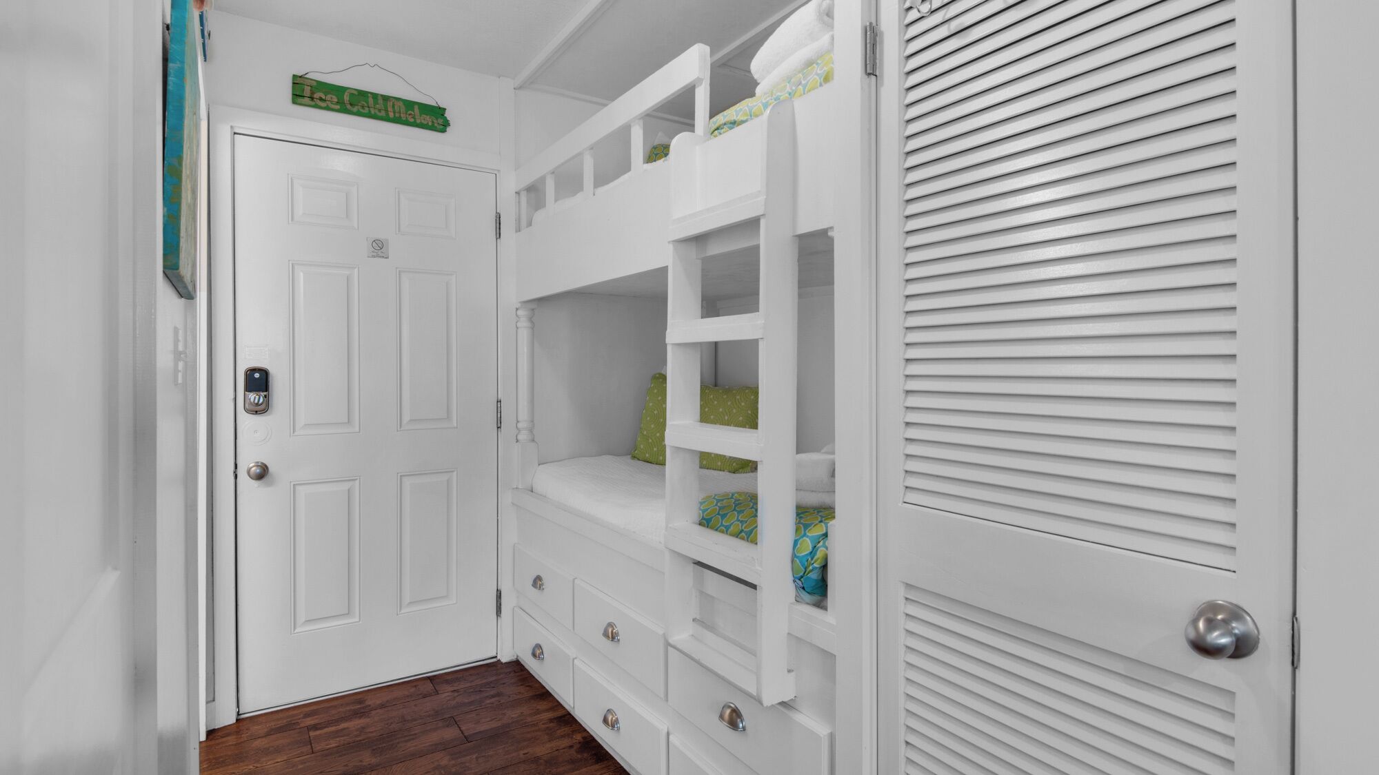 A narrow hallway with a white door, a white built-in bench with storage drawers, and a white closet with horizontal blinds.