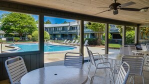 Un espacio al aire libre techado con piscina, sillones de descanso y mesas.
