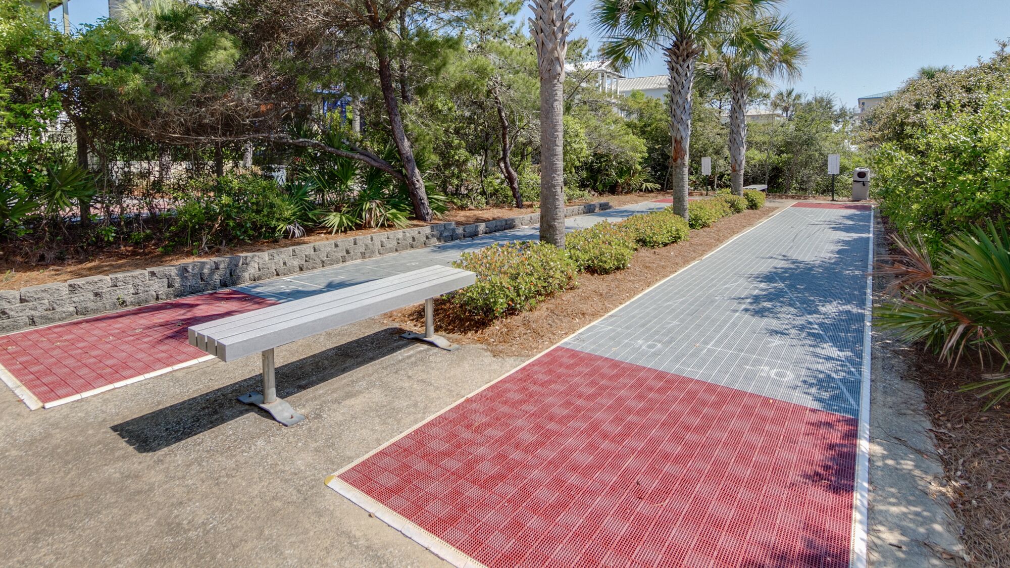 A pathway with red and blue tactile paving, a bench, and a stone wall with greenery.