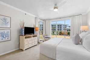 Habitación de hotel con una cama grande, un televisor en un mueble de madera, una silla y un balcón con vistas a edificios.