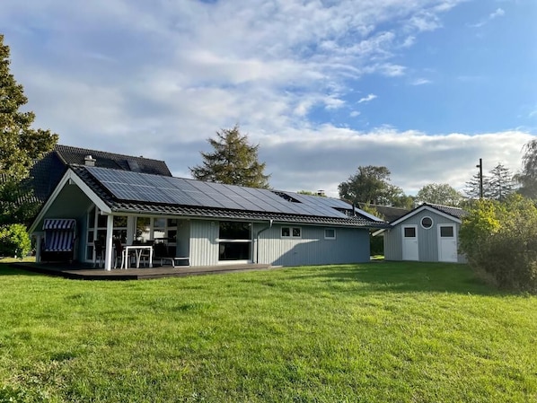 A house with a solar panel roof, a covered porch, and a small shed.