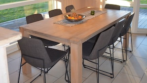Un espace de salle à manger moderne avec une table en bois, des chaises noires et des luminaires suspendus.