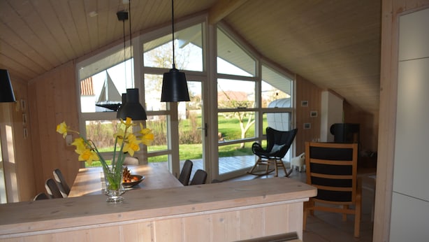 Une cuisine moderne dotée de grandes fenêtres, de meubles en bois et d’un coin repas avec des chaises.