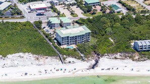Une vue aérienne d’un hôtel situé sur la côte, avec plusieurs étages, donnant sur la plage, et dont on peut apercevoir la piscine.