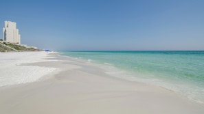 Une plage avec un ciel dégagé, un rivage sablonneux et un immeuble à plusieurs étages situé sur la gauche.