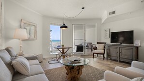 Una sala de estar con un sofá, una mesa de centro de vidrio, un televisor y un balcón con vistas.