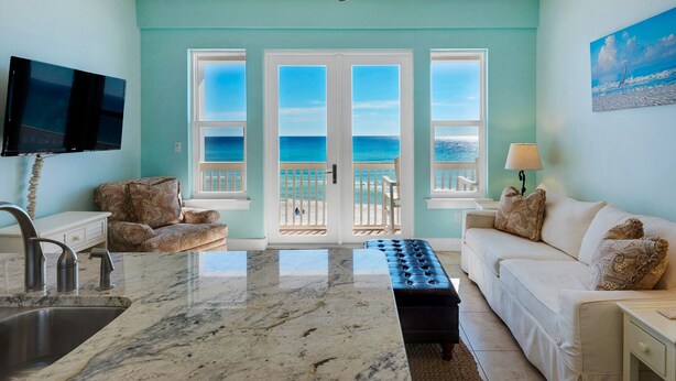 A room with a kitchen area, a dining table, and a sofa. There are three doors leading to a balcony with a view of the ocean. - Gulf Front in Seagrove ~ Amazing Views + Free Attraction Tickets! (Santa Rosa Beach)