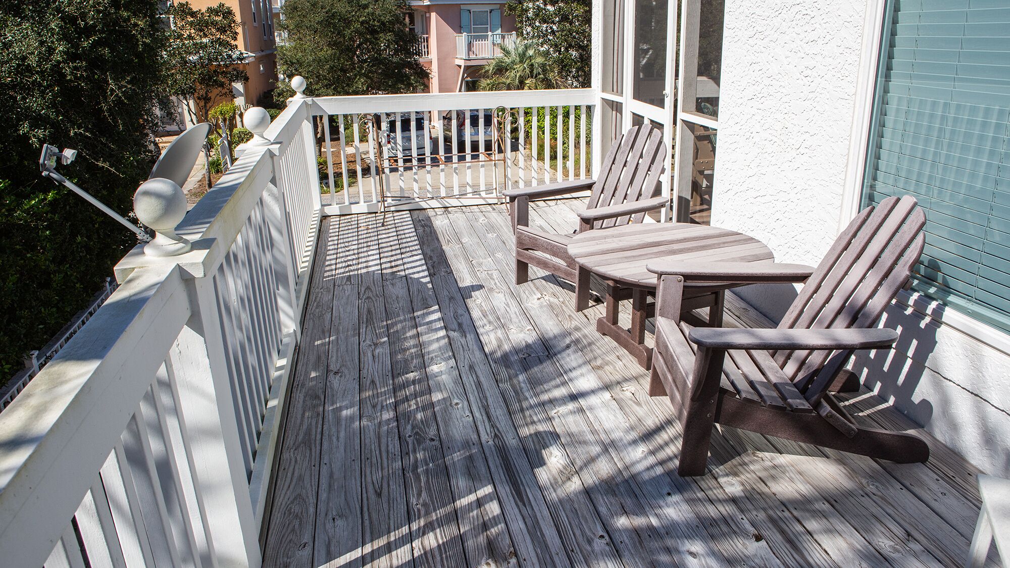 A wooden deck with a white railing, two Adirondack chairs, and a small table.