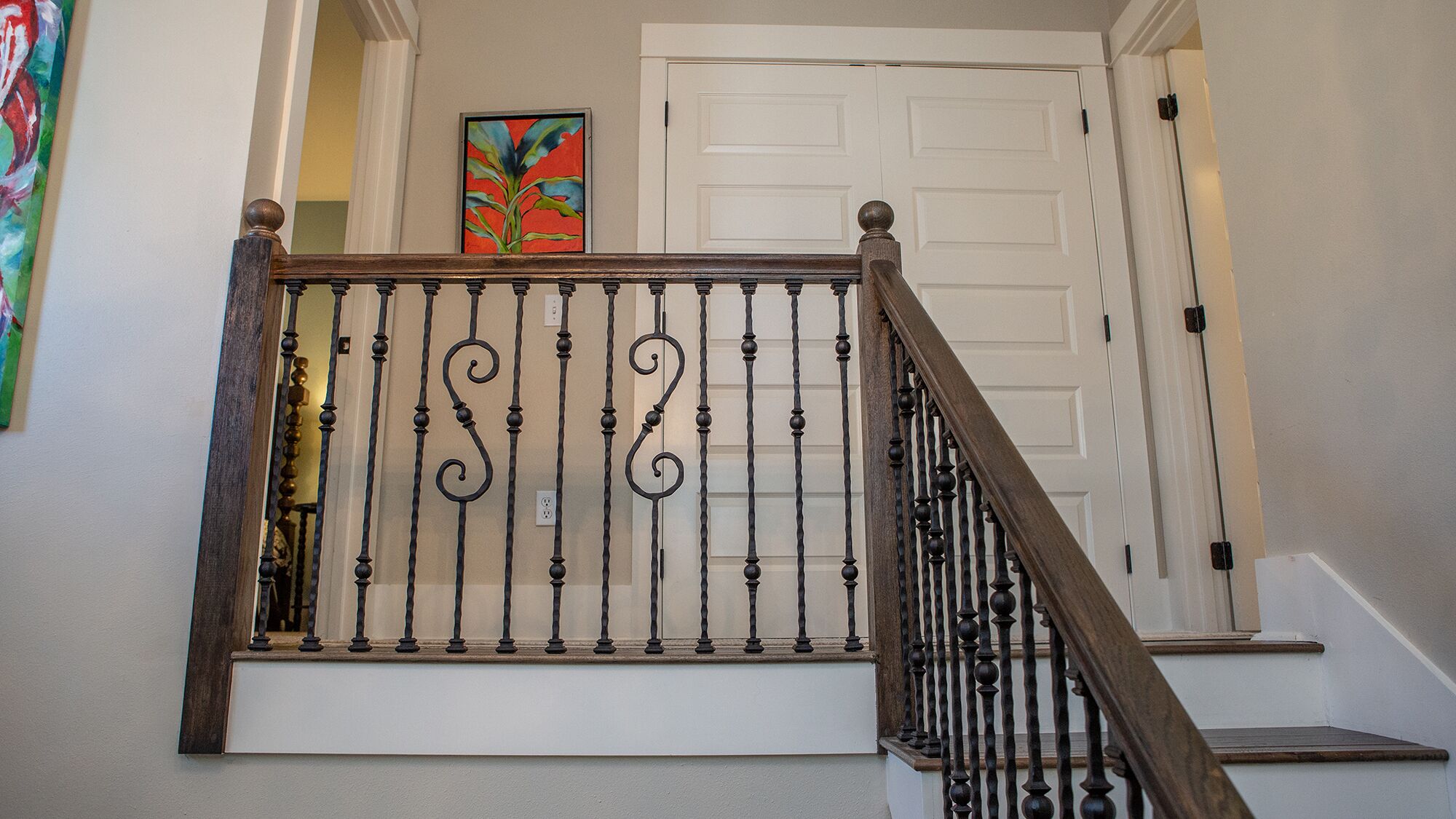 Eine Treppe mit einem Holzgeländer und schwarzen Metallspindeln mit ornamentalem Volutenelement.