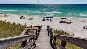 Eine Holztreppe führt zu einem Strand mit Sonnenschirmen und Liegestühlen.