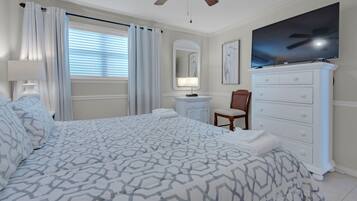 A neatly arranged bedroom with a bed, a dresser, a television, and a window with curtains.