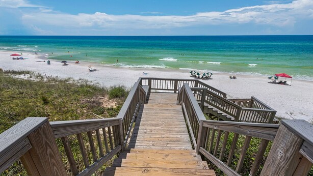 A wooden staircase leading to a beach with white sand and turquoise water.