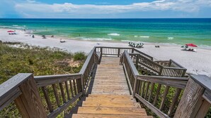 Una escalera de madera que lleva a una playa con agua turquesa cristalina y arena blanca.