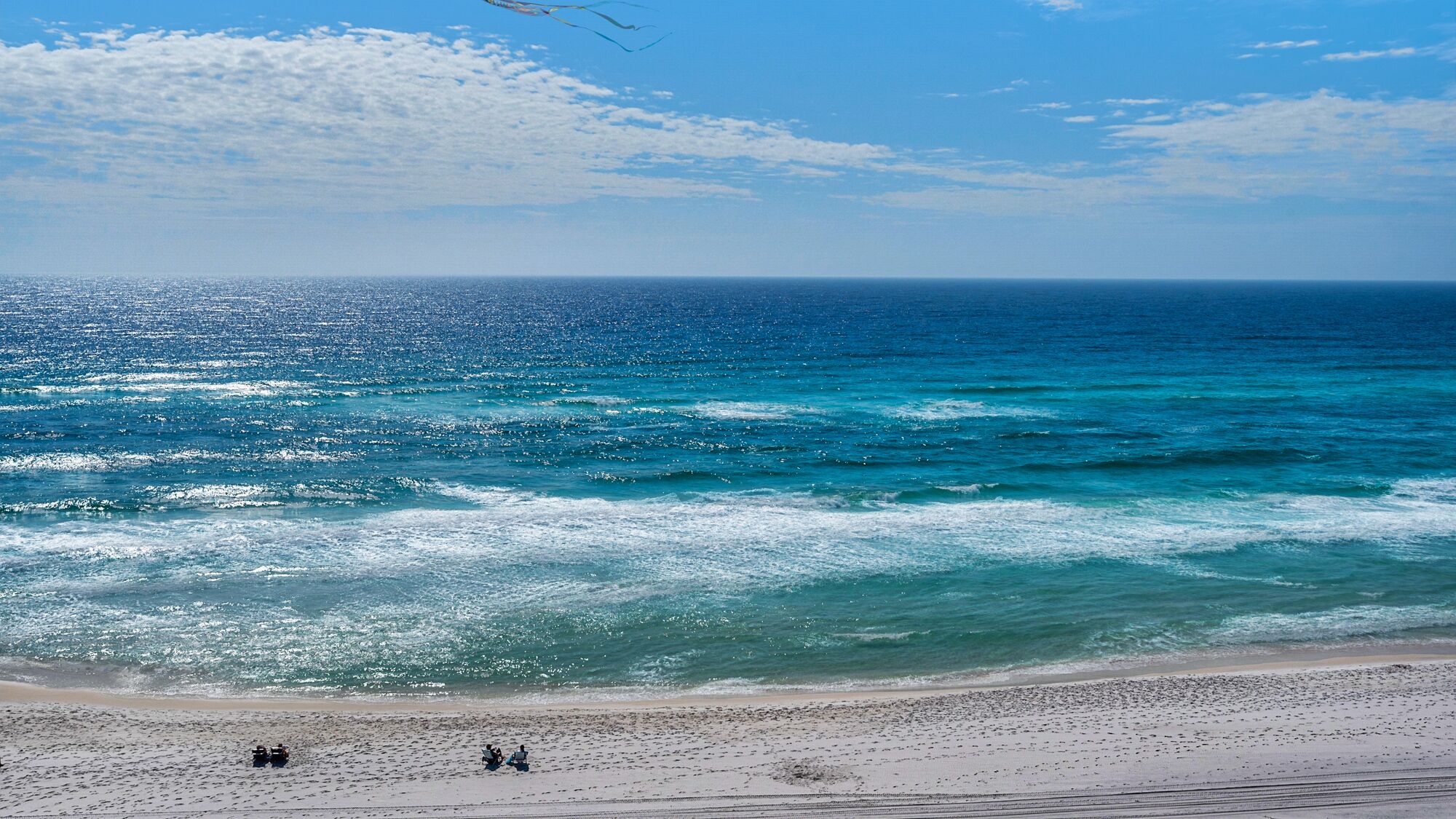A beach with a clear view of the ocean and a few people on the sand.