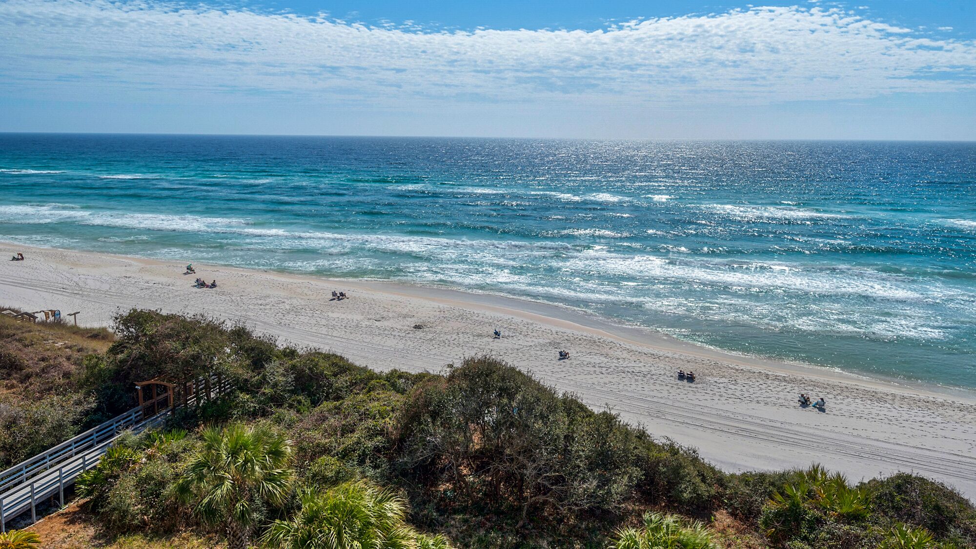 A beach with a clear view of the ocean, a sandy shore, and some vegetation in the foreground.
