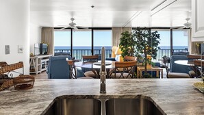 Una cocina moderna con un amplio ventanal con vista al mar, un comedor con mesa y sillas, y un balcón con vistas al océano.