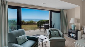 Une chambre d’hôtel avec balcon donnant sur l’océan, comprenant deux fauteuils, une petite table et une lampe.