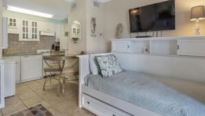 Una habitación compacta con cama, una pequeña mesa de comedor, zona de cocina y televisor.