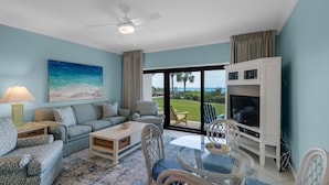 Un salon comprenant un canapé, des fauteuils, une table basse, un téléviseur et un balcon avec vue sur l’océan.