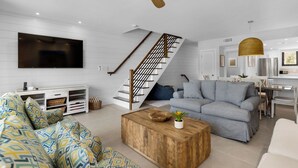 A modern living room with a staircase, a flat-screen TV, a wooden coffee table, and a dining area.