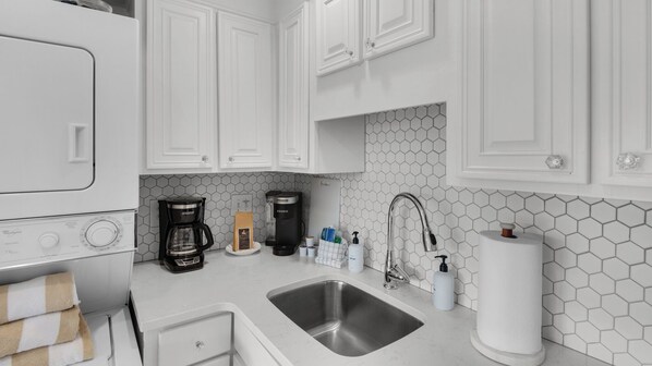 A modern kitchen with white cabinets, a stainless steel sink, a coffee maker, and a kettle.