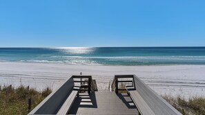 A wooden boardwalk leading to a beach with clear blue water and a sandy shore.