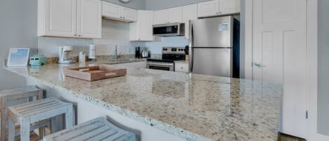 A modern kitchen with white cabinetry, granite countertops, stainless steel appliances, and a small island with stools.