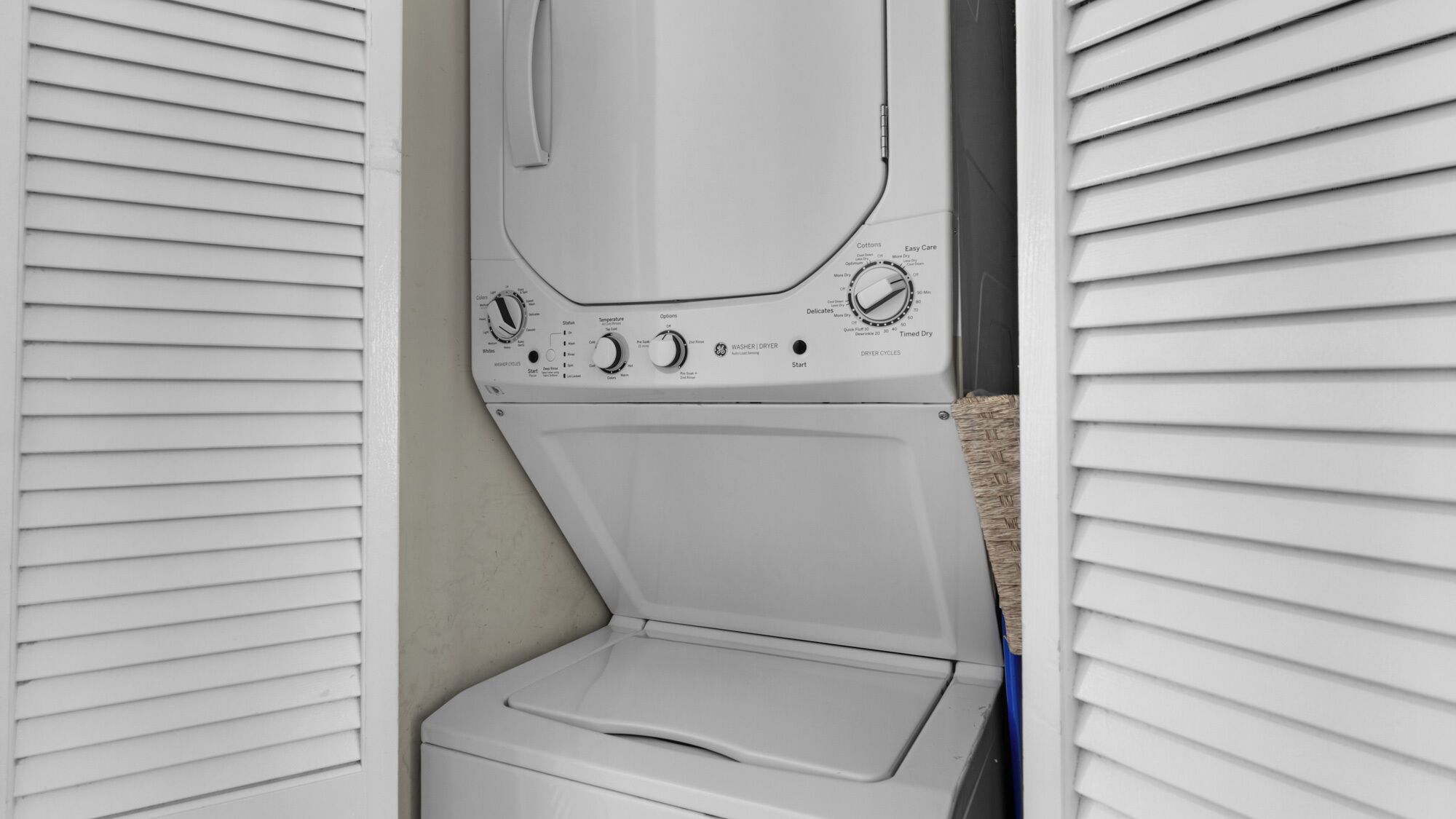 Vista frontal de una unidad de lavadora y secadora blanca instalada en un cuarto de lavado con paredes exteriores blancas y piso color beige.
