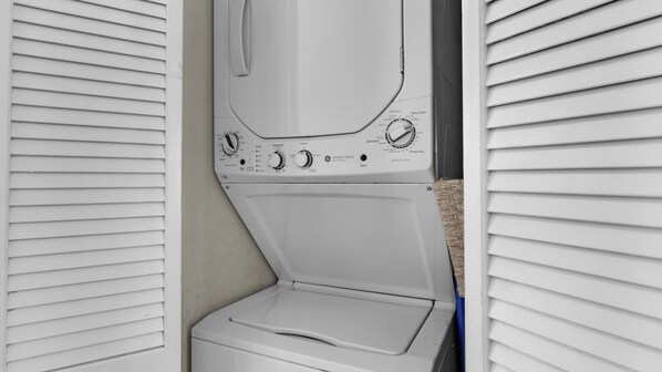 Vista frontal de una unidad de lavadora y secadora blanca instalada en un cuarto de lavado con paredes exteriores blancas y piso color beige.