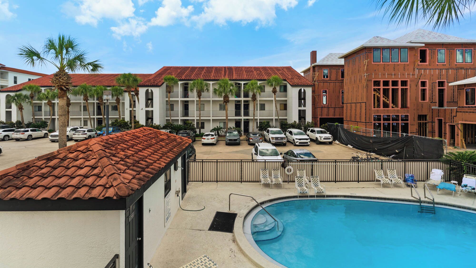 A hotel with a swimming pool, multiple balconies, and parked cars.