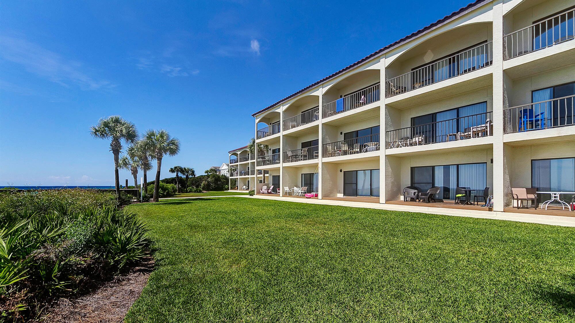 A multi-story hotel with balconies, a well-maintained lawn, and palm trees.