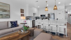 Una cocina moderna con armarios blancos, un refrigerador de acero inoxidable y un microondas. Hay un comedor con sillas y una mesa blancos.